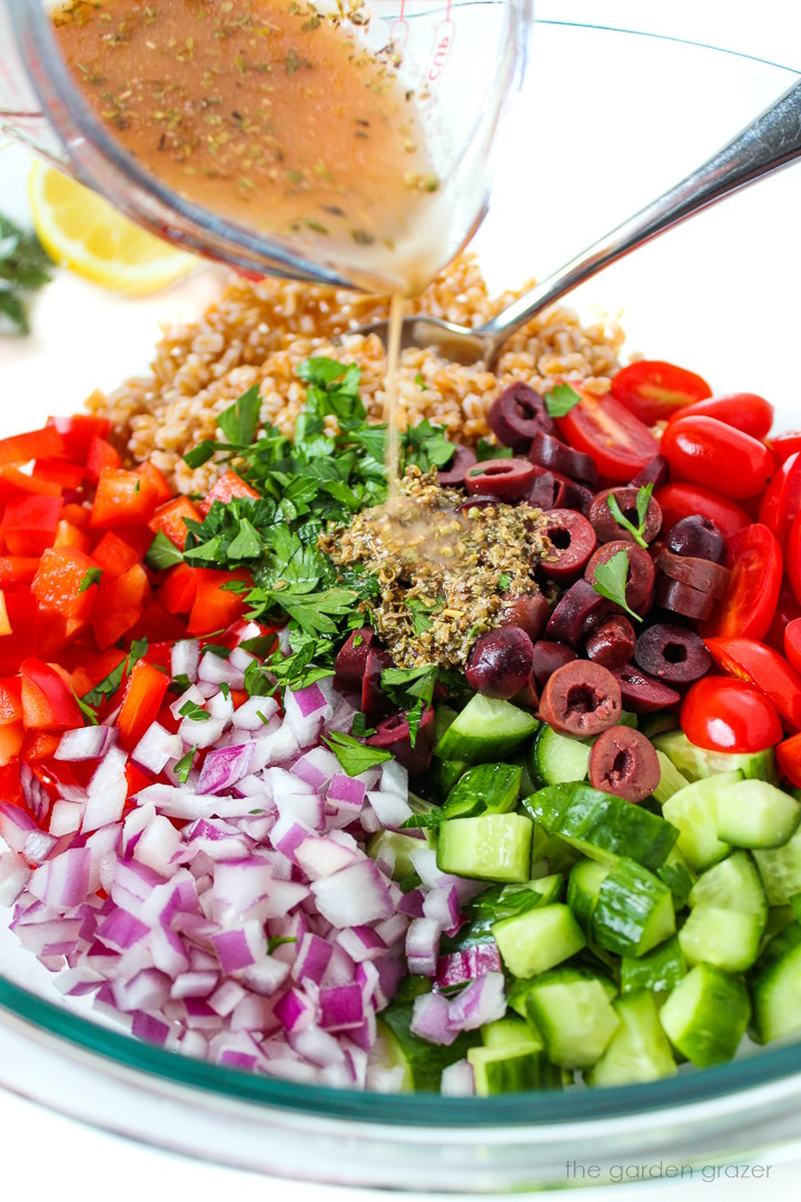 Lemon vinegar dressing being poured over a Greek Farro Salad in a glass bowl