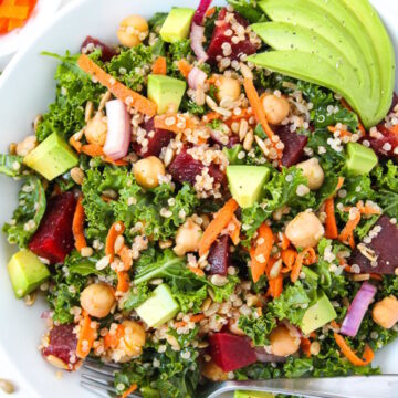 Kale superfood power salad with avocado, beets, and garbanzo beans on a white plate with serving fork