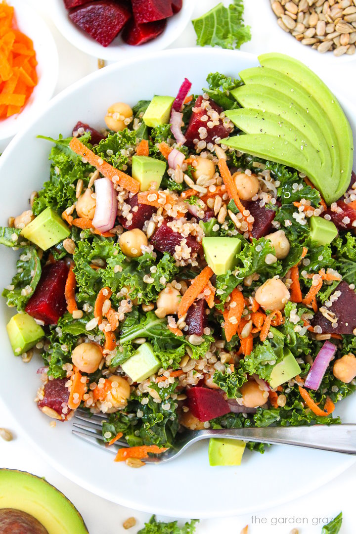 Kale superfood power salad with avocado, beets, and garbanzo beans on a white plate with serving fork
