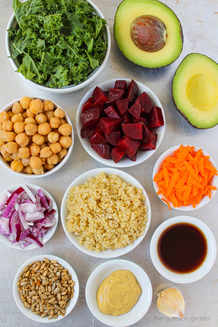 Cooked quinoa, beets, avocado, kale, onion, carrot, and dressing ingredients laid out on a metal tray