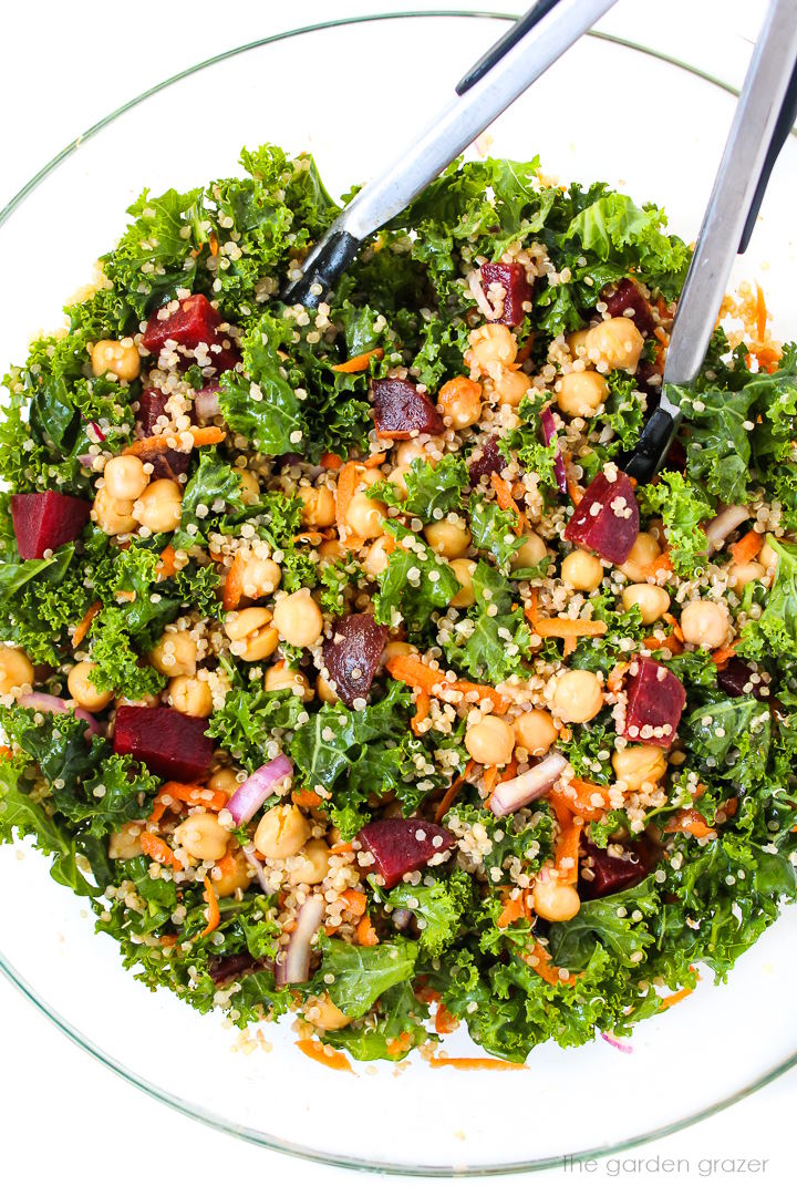 Overhead view of kale superfood power salad mixed together in a large glass bowl with tongs