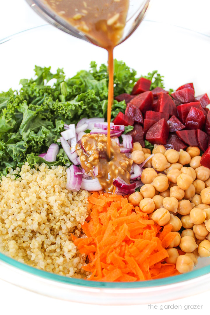 Pouring balsamic dressing on kale salad ingredients in a large glass bowl