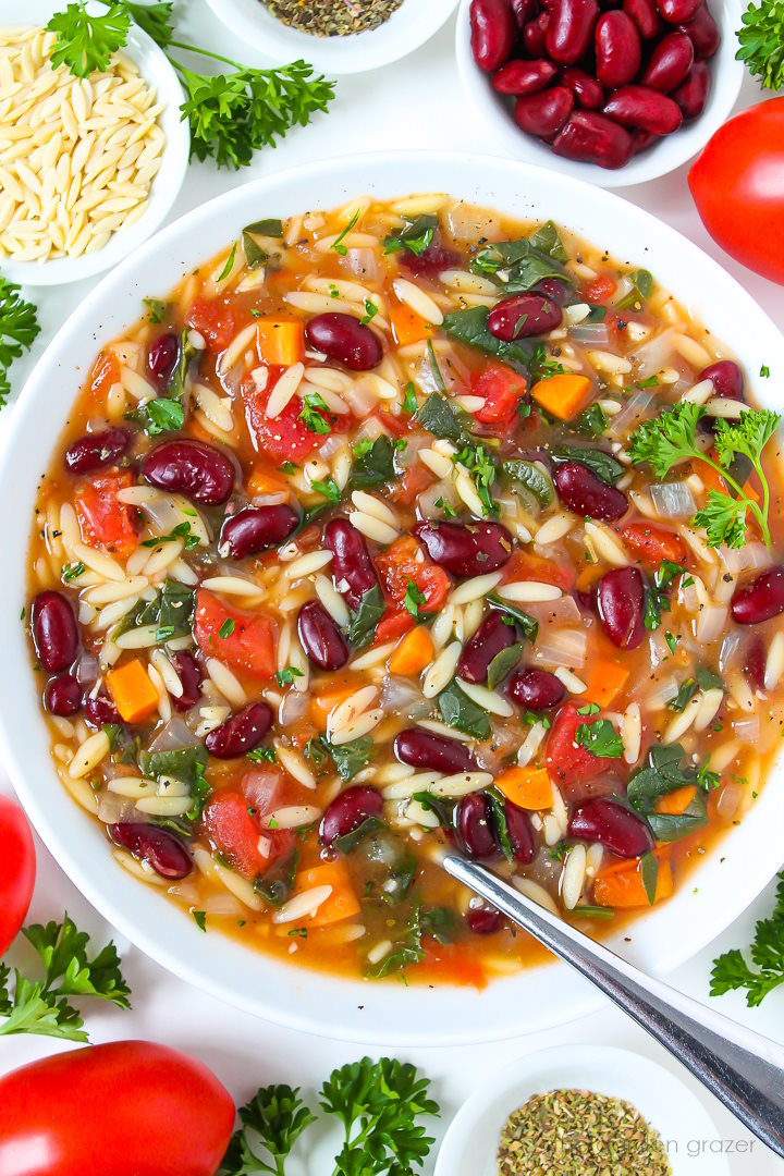 Overhead view of kidney bean soup with orzo and spinach in a white bowl with spoon