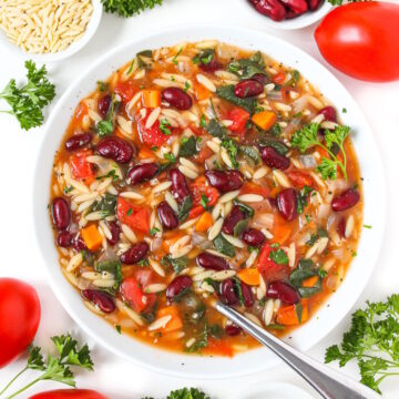 A white bowl of vegan kidney bean, spinach, orzo soup garnished with fresh parsley