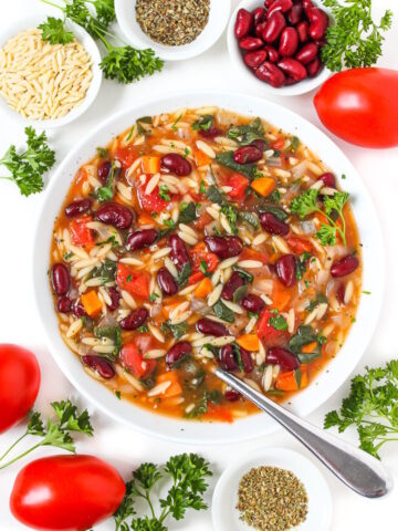 A white bowl of vegan kidney bean, spinach, orzo soup garnished with fresh parsley