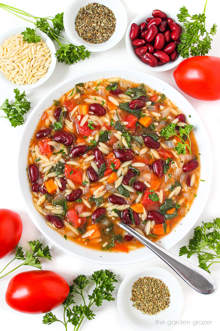 A white bowl of vegan kidney bean, spinach, orzo soup garnished with fresh parsley