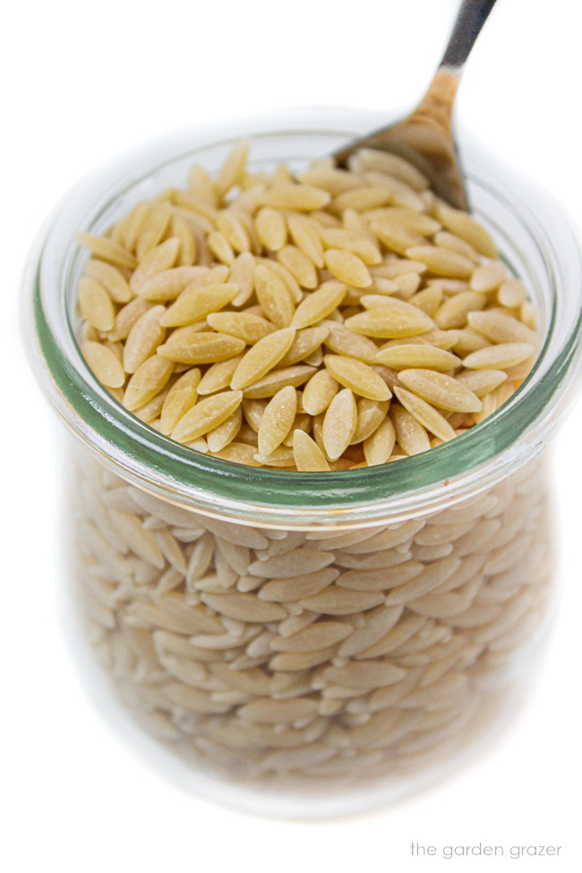 Uncooked orzo pasta in a small jar with spoon