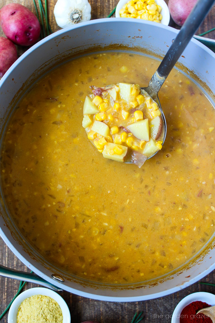 A ladle lifting up some vegan potato corn chowder from a large pot after cooking
