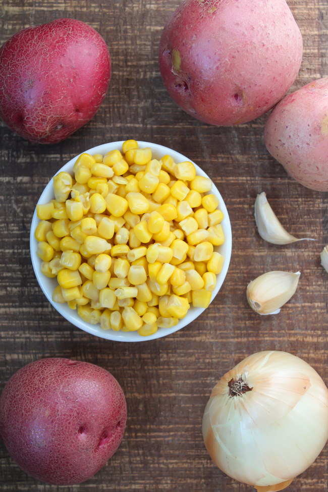 Red potatoes, sweet corn, onion, and garlic on a wooden table