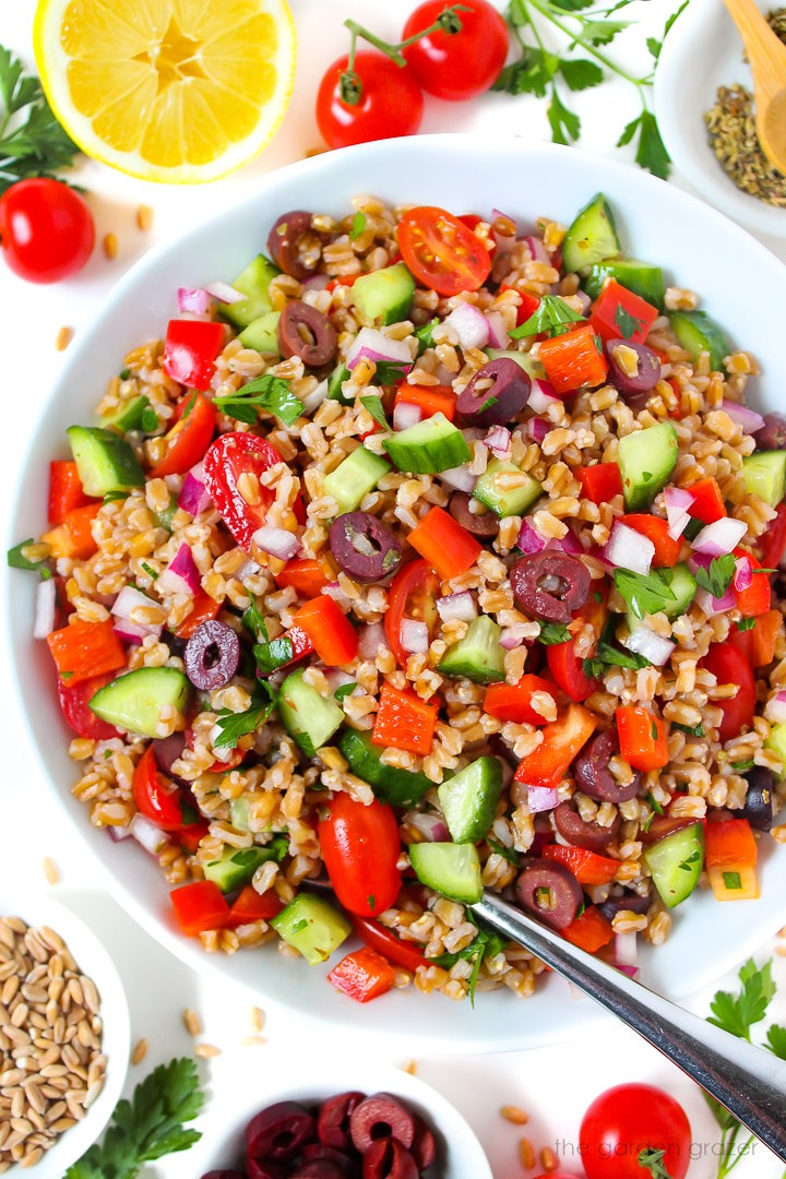 Vegan Greek Farro Salad in a large white bowl with serving spoon