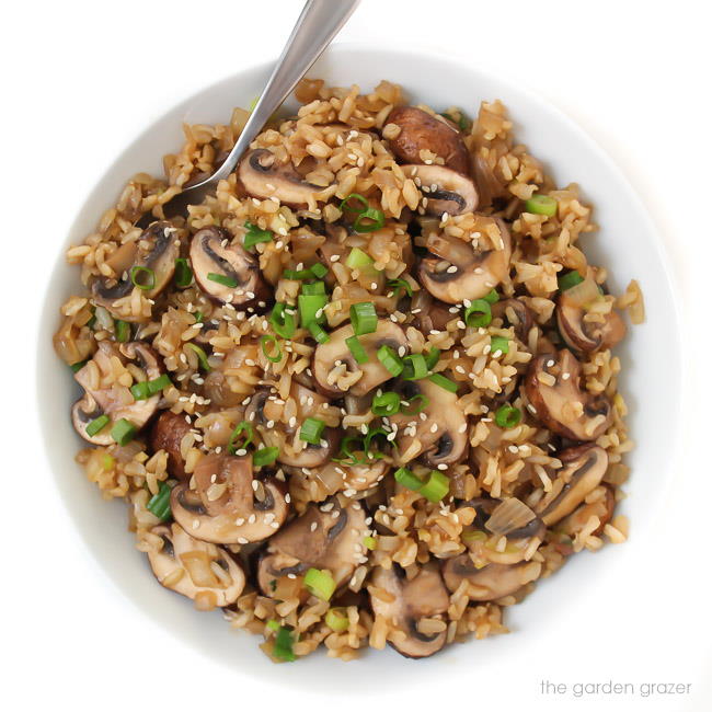 Cooked brown rice in a bowl with spoon garnished with sesame seeds