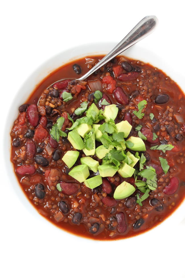 Lentil Chili in a white bowl with spoon and avocado on top