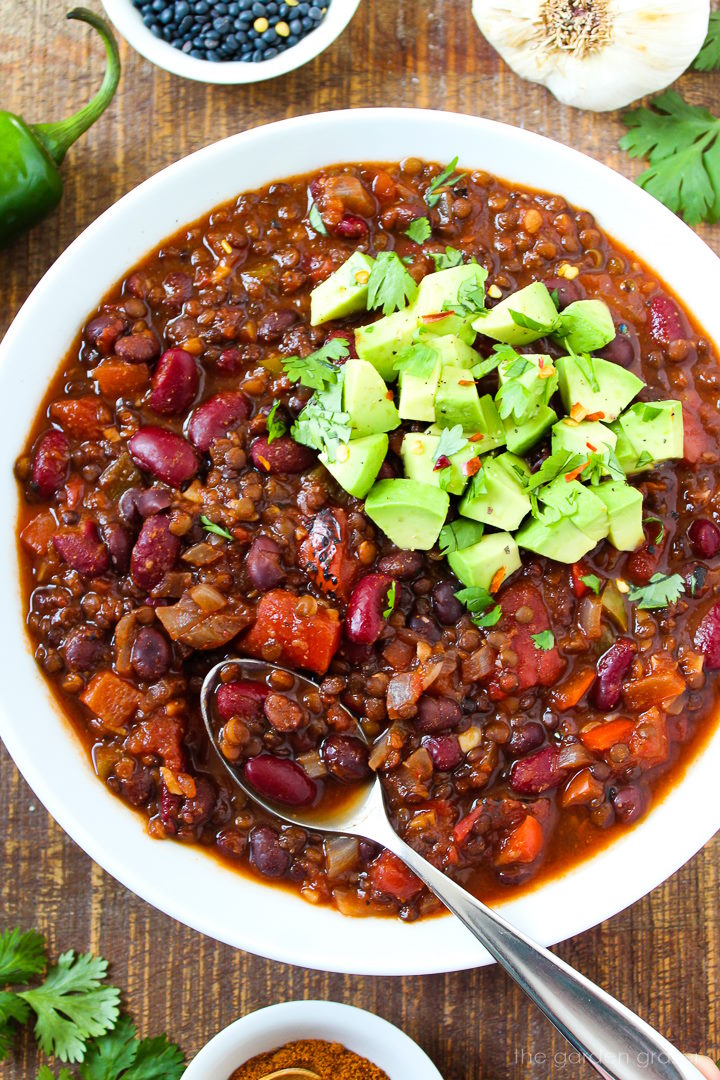 Close up view of black lentil chili with serving spoon topped with avocado and cilantro
