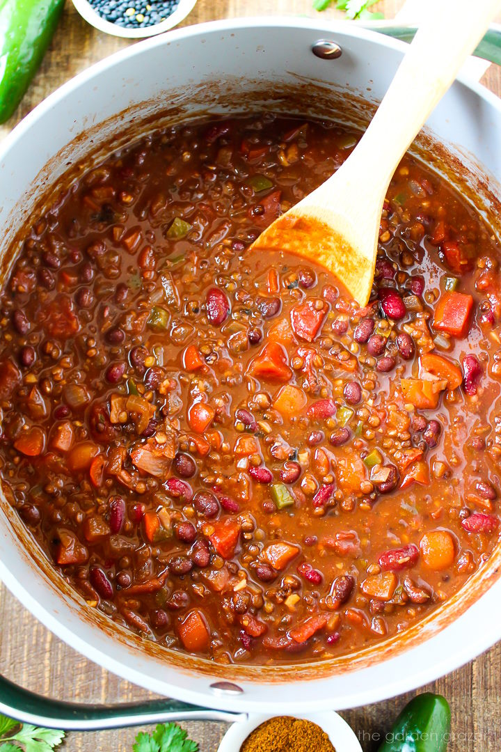 Black lentil chili cooking in a large pot with wooden stirring spoon