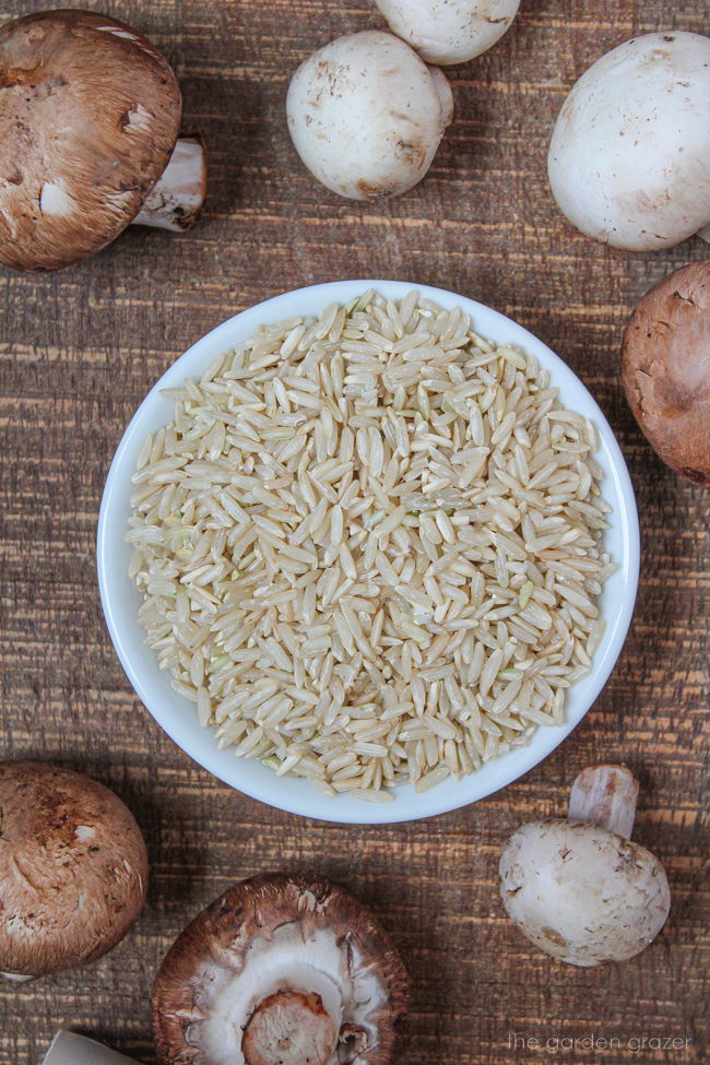 Cremini mushrooms and uncooked brown rice on a wooden table