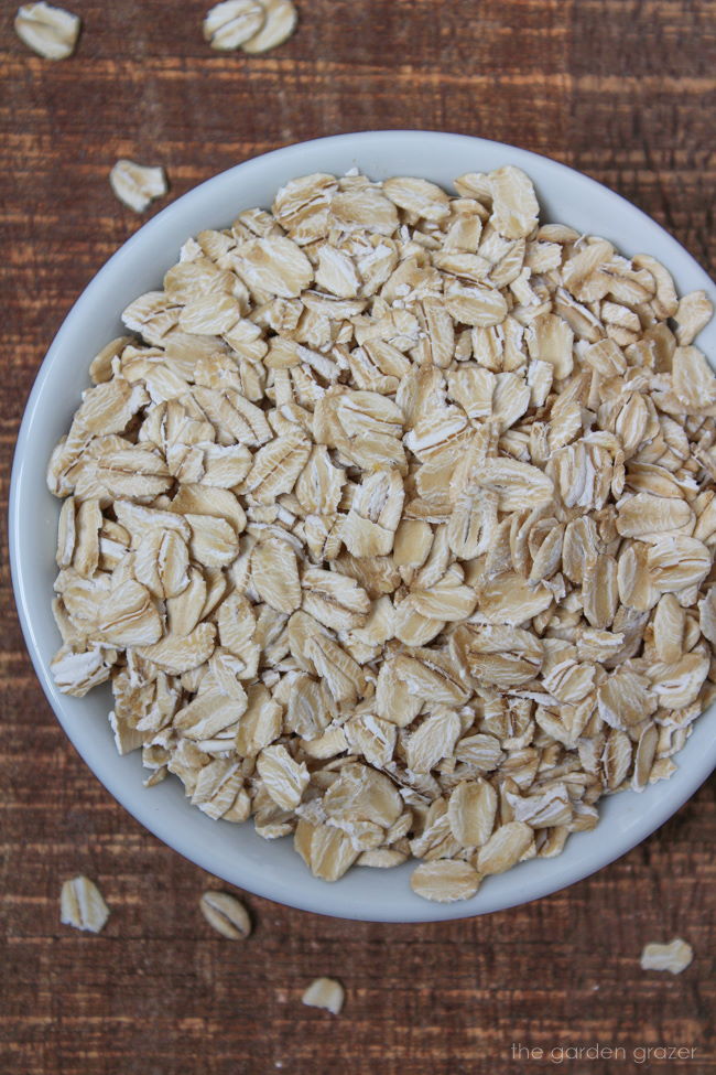 Raw rolled old fashioned oats in a small white bowl on a wooden table