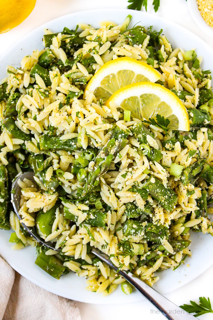 Close-up view of lemon asparagus orzo in a white bowl with serving spoon