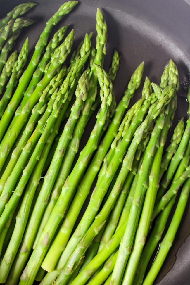 Fresh asparagus spears steaming in a pan on the stove