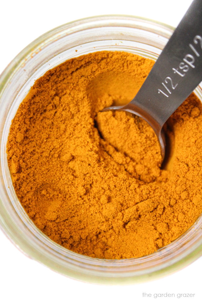 Ground turmeric in a small glass jar with measuring spoon