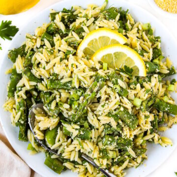 Overhead view of asparagus orzo in a white bowl with fresh lemon slices on top