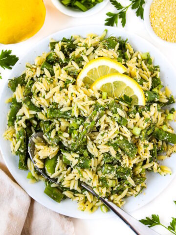 Overhead view of asparagus orzo in a white bowl with fresh lemon slices on top