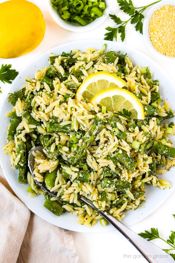 Overhead view of asparagus orzo in a white bowl with fresh lemon slices on top