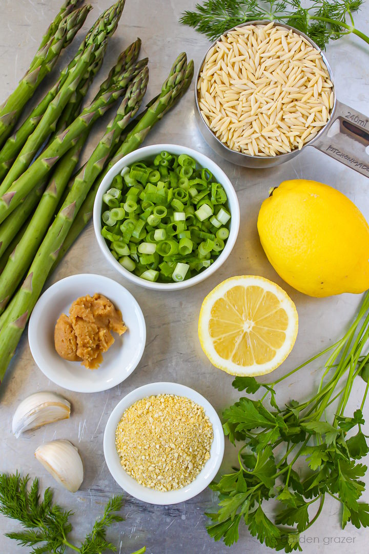 Fresh asparagus, lemons, green onions, miso, garlic, lemon, and fresh herb ingredients laid out on a metal tray