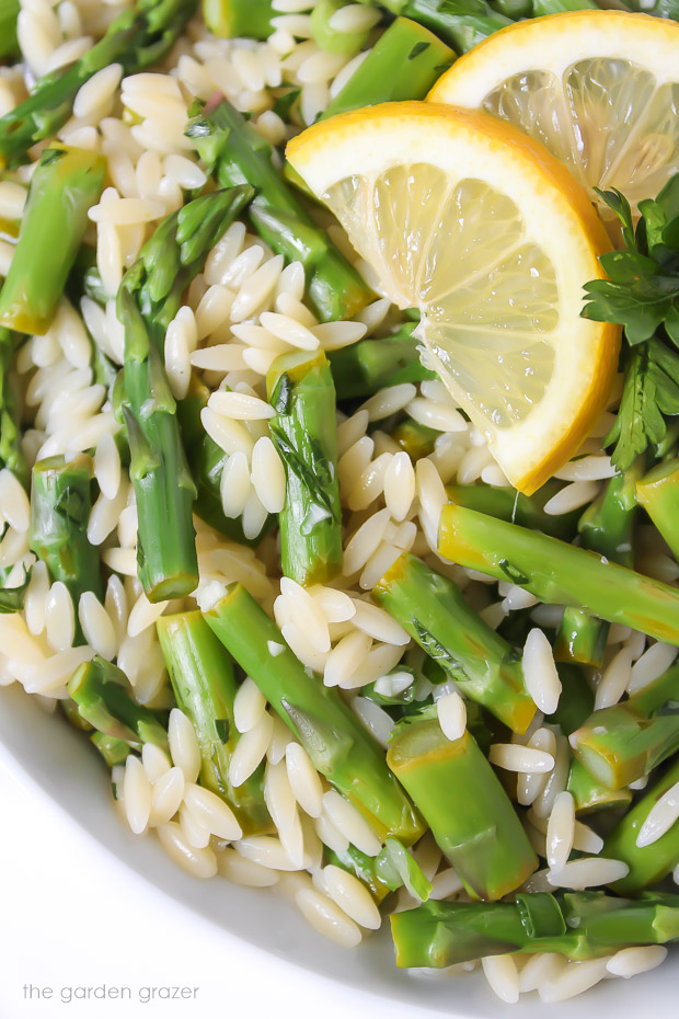 Garlic orzo with asparagus in a bowl topped with lemon slices