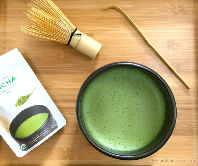 Bowl of whisked matcha sitting on bamboo tray with whisk and scoop