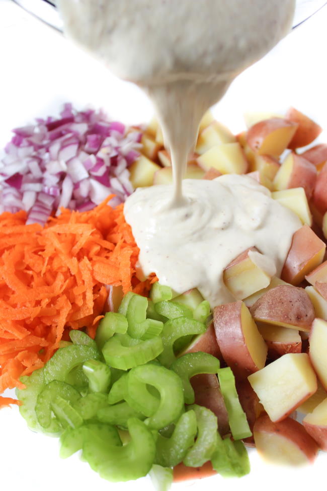 Vegan creamy dressing being poured on to potato salad