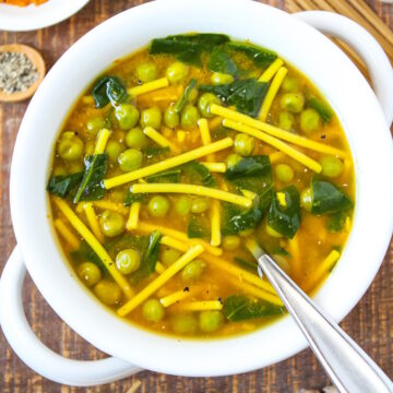 Turmeric noodle soup in a white serving bowl with spoon on a wooden table