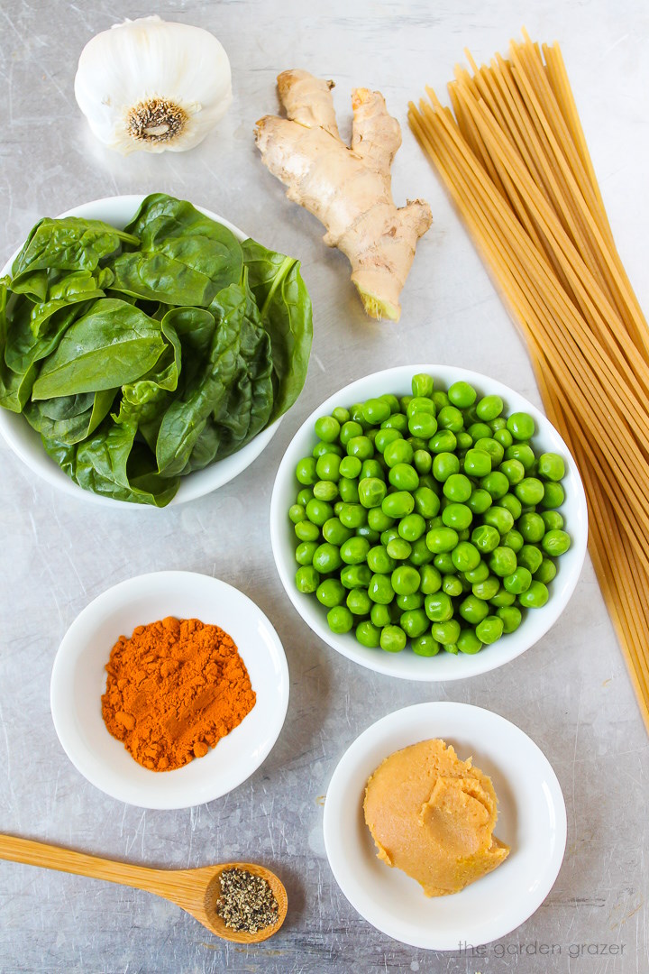 Spaghetti pasta, green peas, garlic, ginger, miso, and spinach ingredients laid out on a metal tray
