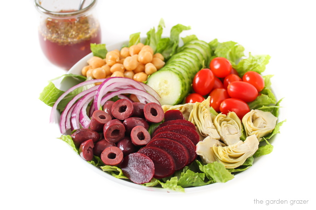 Fresh salad in a white bowl with dressing in a jar