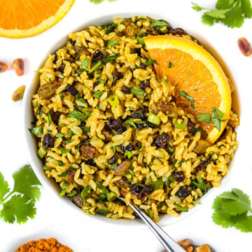 Vegan curried orange rice salad in a white bowl with serving spoon