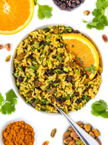 Vegan curried orange rice salad in a white bowl with serving spoon