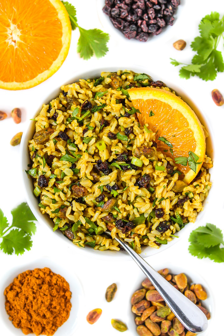 Vegan curried orange rice salad in a white bowl with serving spoon