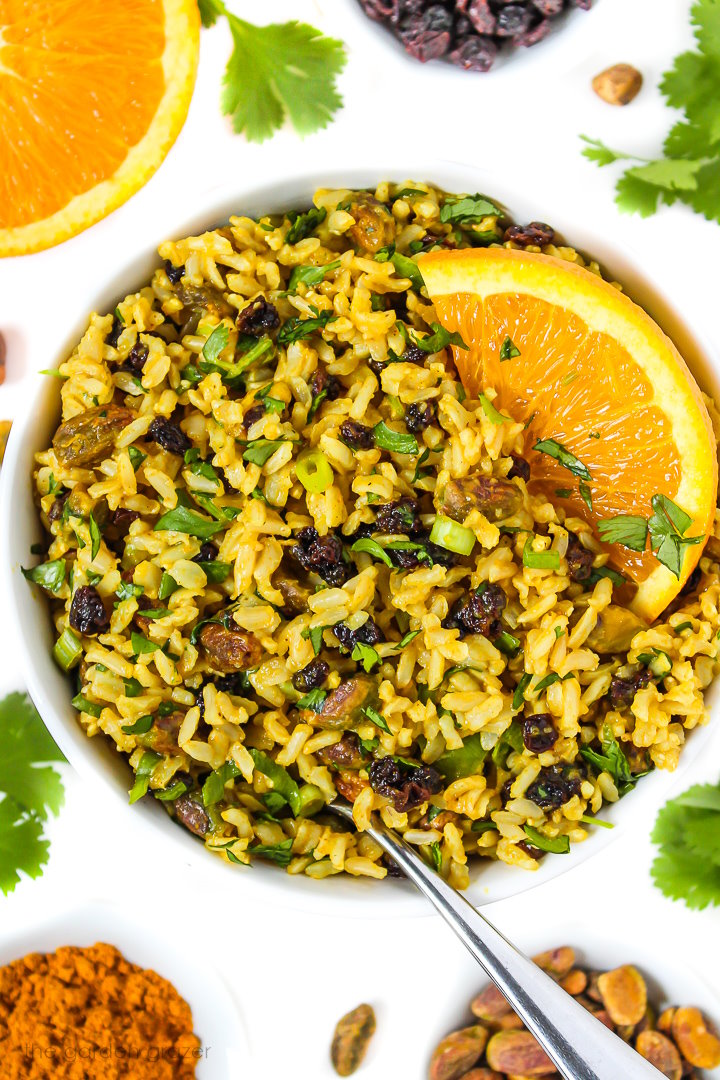 Overhead view of vegan curried rice salad in a white bowl topped with an orange slice