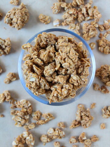 Oil-free peanut butter granola in a glass bowl and scattered around on a tray