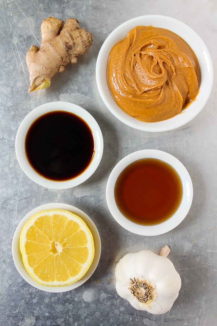 Nut butter, ginger, garlic, lemon, maple syrup, and tamari ingredients laid out on a metal tray