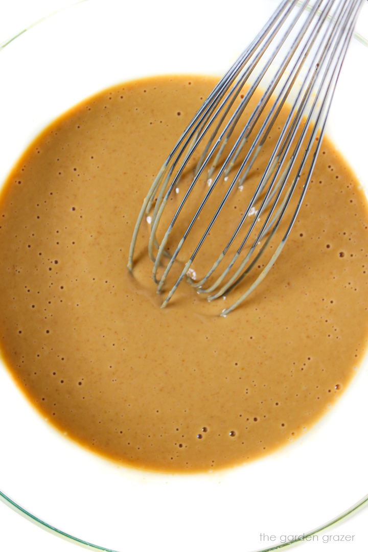 Whisking together vegan peanut sauce in a glass bowl with metal whisk