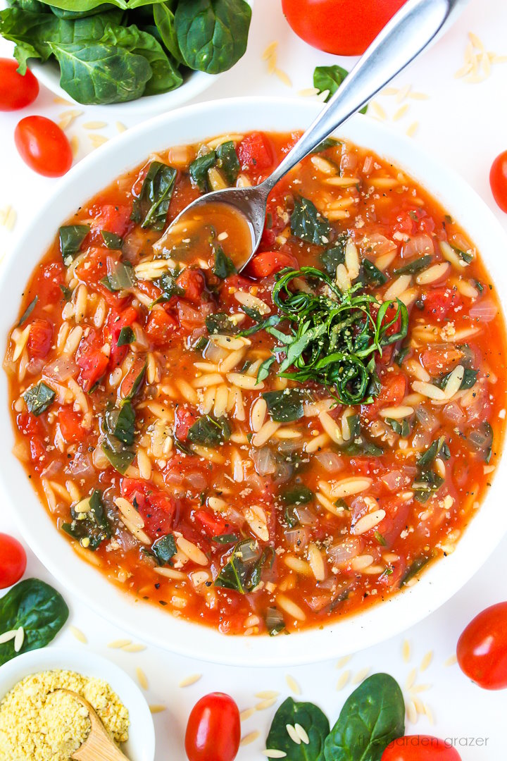 Overhead view of vegan tomato orzo spinach soup in a white bowl with fresh basil
