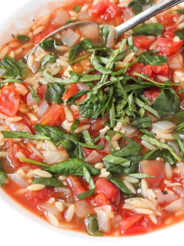Tomato orzo spinach soup in a white bowl with spoon