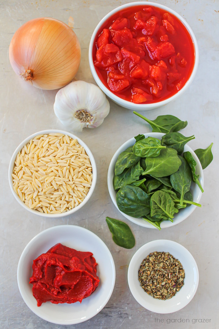 Spinach, tomatoes, onion, garlic, tomato paste, and herb ingredients laid out on a metal tray