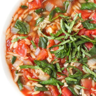 Bowl of tomato orzo spinach soup topped with fresh basil