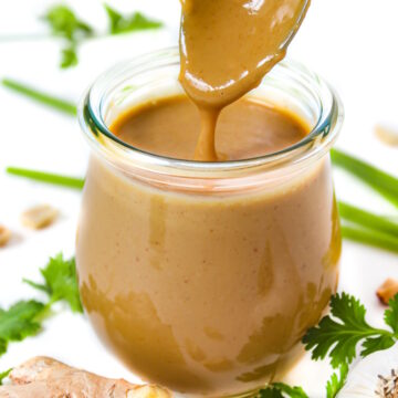 Vegan peanut sauce in a small glass jar with serving spoon