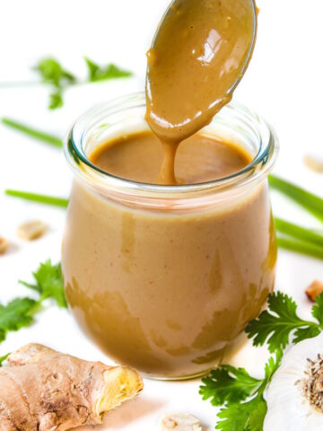 Vegan peanut sauce in a small glass jar with serving spoon