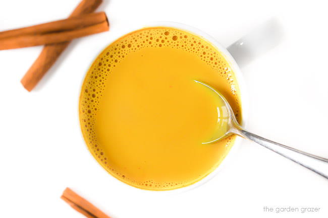 Mug of turmeric milk latte with cinnamon sticks and a spoon