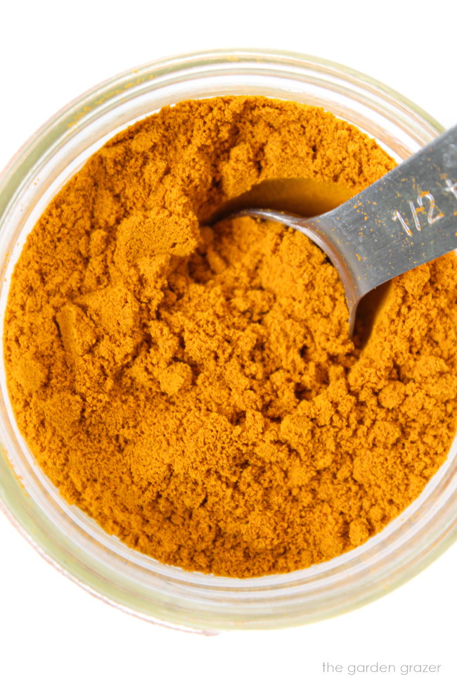 Ground turmeric in a small glass jar with metal teaspoon