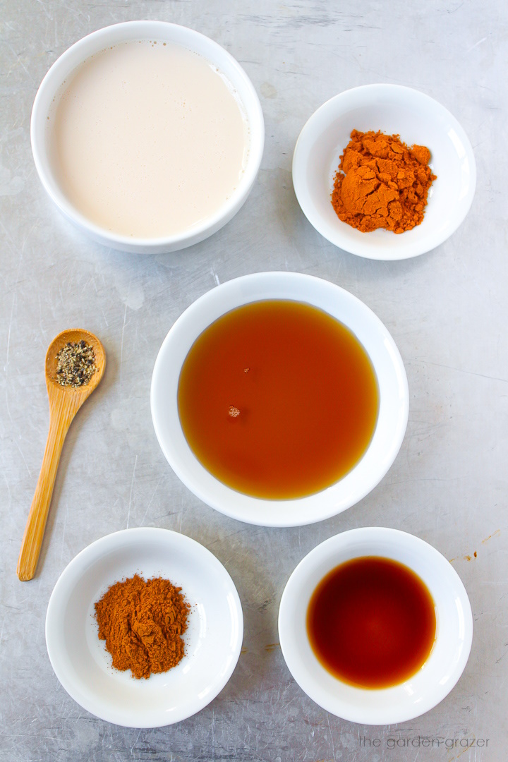 Ground turmeric, soy milk, maple syrup, cinnamon, vanilla, and black pepper ingredients laid out on a metal tray
