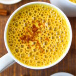 Overhead view of vegan golden milk latte sprinkled with cinnamon in a white mug